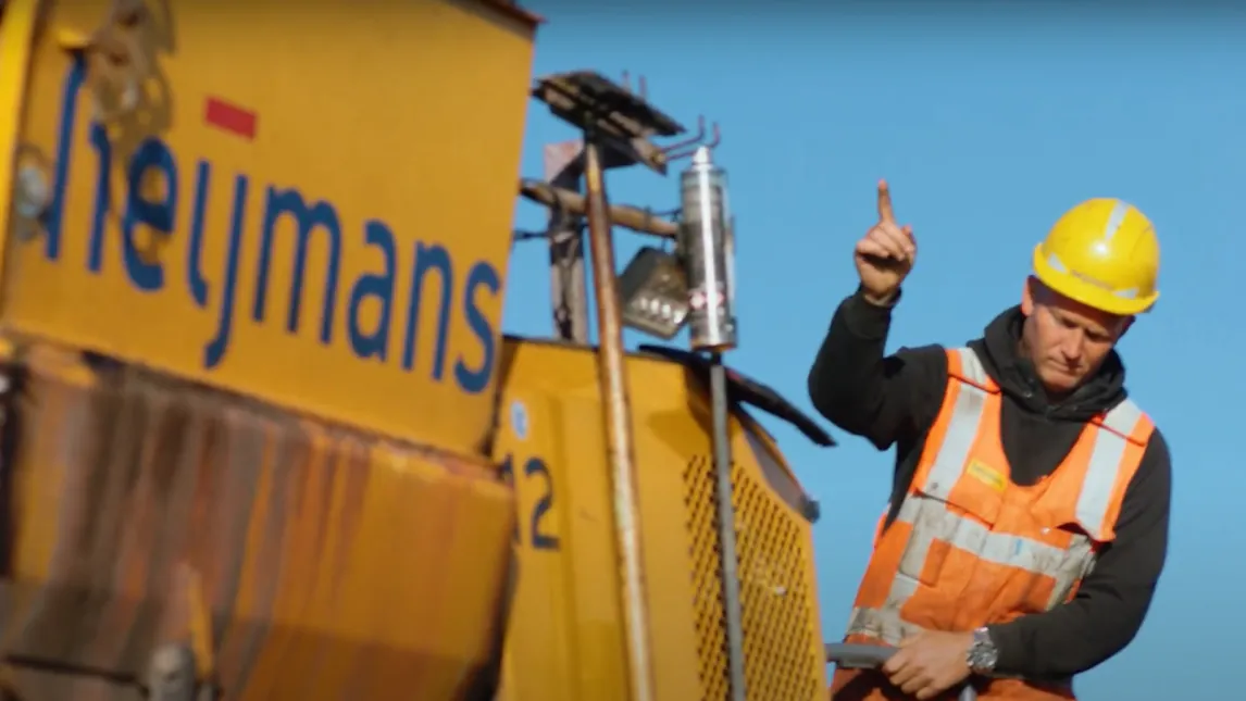 Bouwvakker van Heijmans met helm naast een geel Heijmans-voertuig